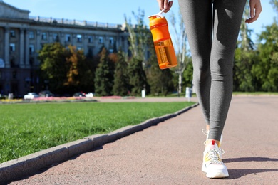 Photo of Young woman holding bottle with clean water on street. Space for text