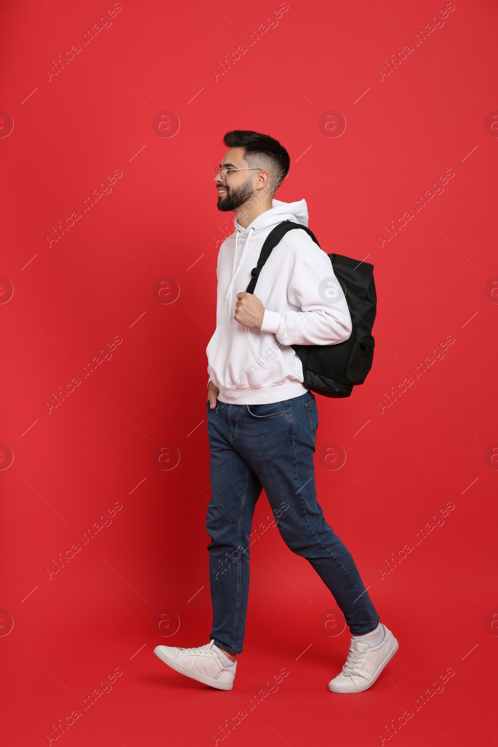 Photo of Young man with stylish backpack walking on red background