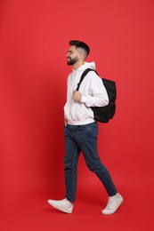 Young man with stylish backpack walking on red background
