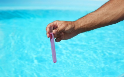 Photo of Man holding test tube with reagent near swimming pool, closeup