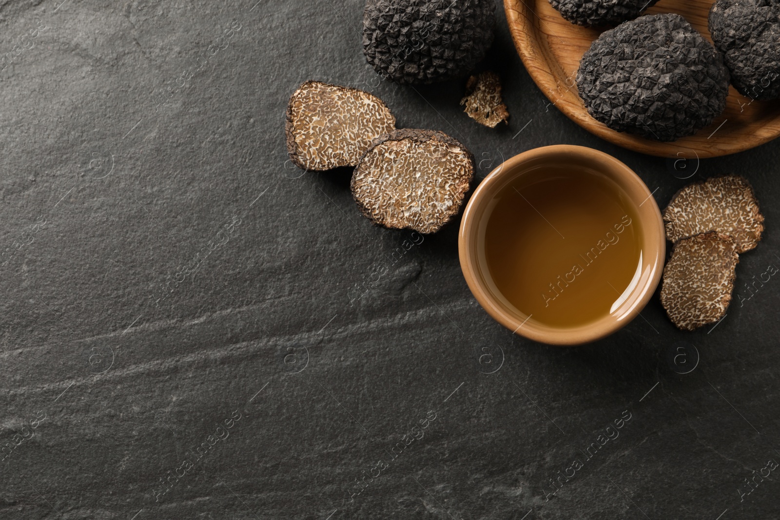 Photo of Bowl of truffle oil on grey table, flat lay. Space for text