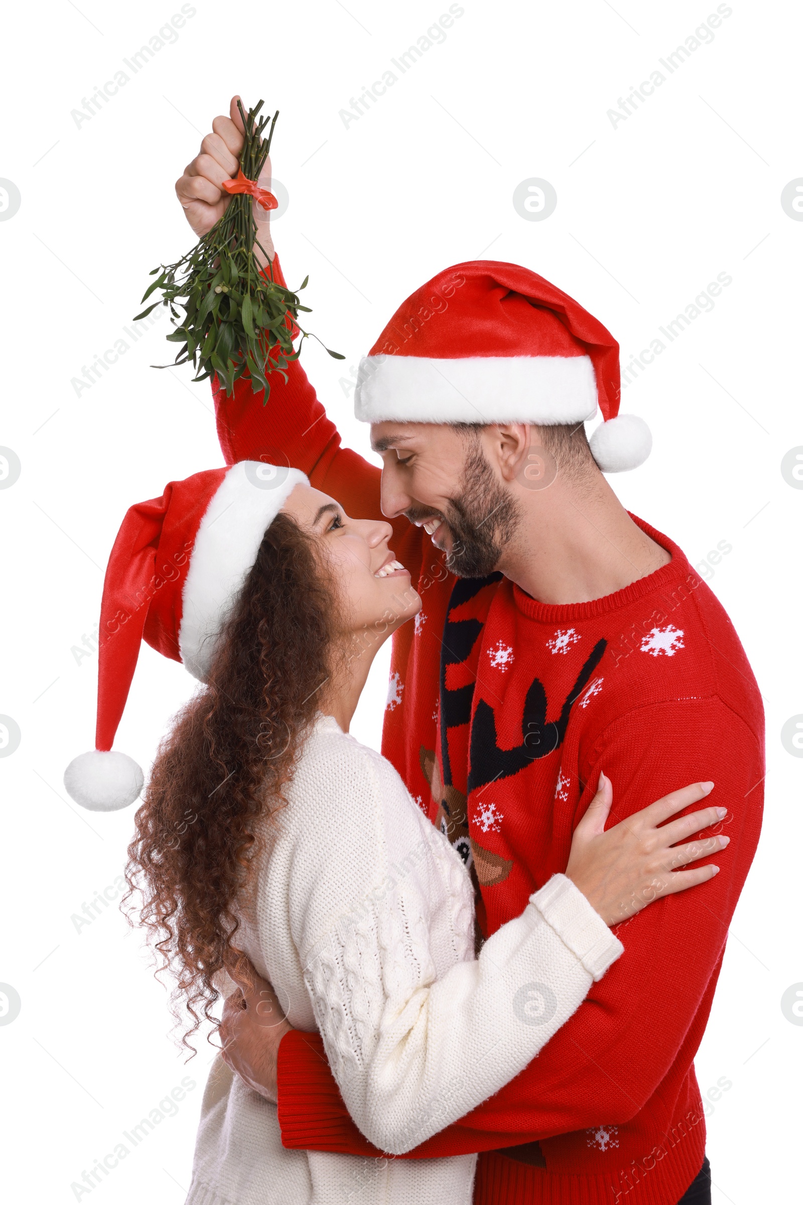 Photo of Lovely couple in Santa hats under mistletoe bunch on white background