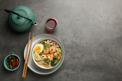 Delicious ramen with shrimps in bowl served on grey table, flat lay with space for text. Noodle soup