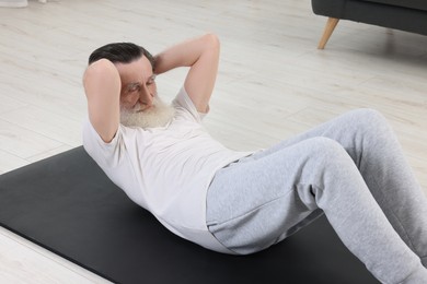 Photo of Senior man in sportswear doing exercises on fitness mat indoors