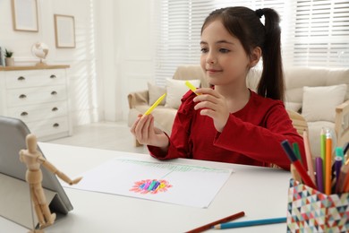 Photo of Little girl drawing on paper with marker at online lesson indoors. Distance learning