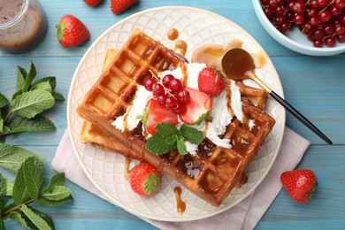 Photo of Delicious Belgian waffles with berries and caramel sauce served on turquoise wooden table, flat lay