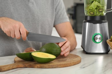 Man cutting avocado for delicious smoothie at white marble table in kitchen, closeup