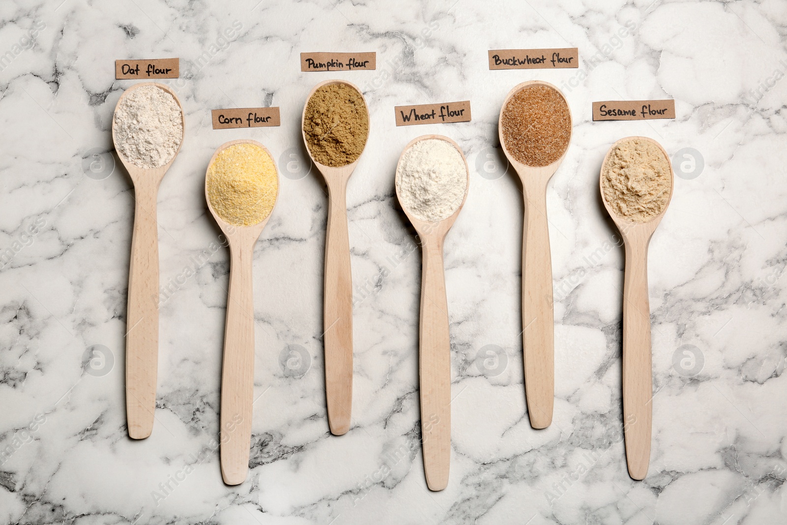 Photo of Spoons with different types of flour and tags on marble background, top view