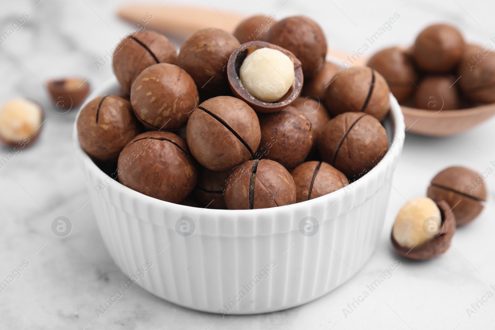 Photo of Tasty Macadamia nuts in bowl on white table, closeup