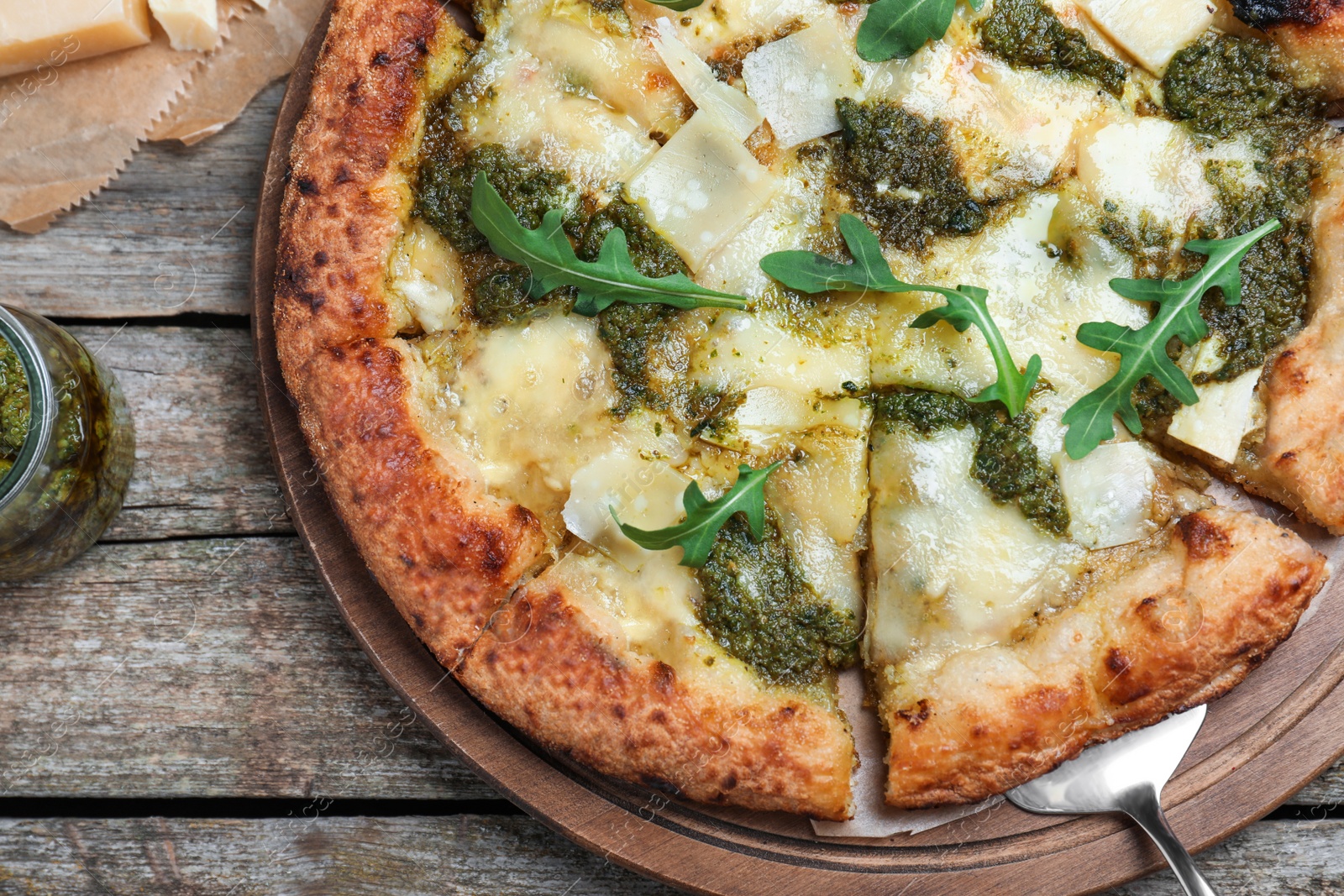 Photo of Delicious pizza with pesto, cheese and arugula on wooden table, flat lay