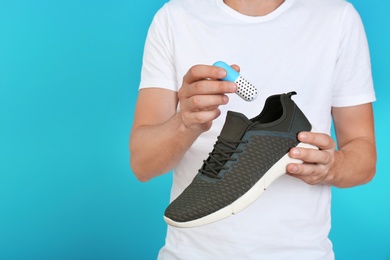 Man putting capsule shoe freshener in footwear on color background