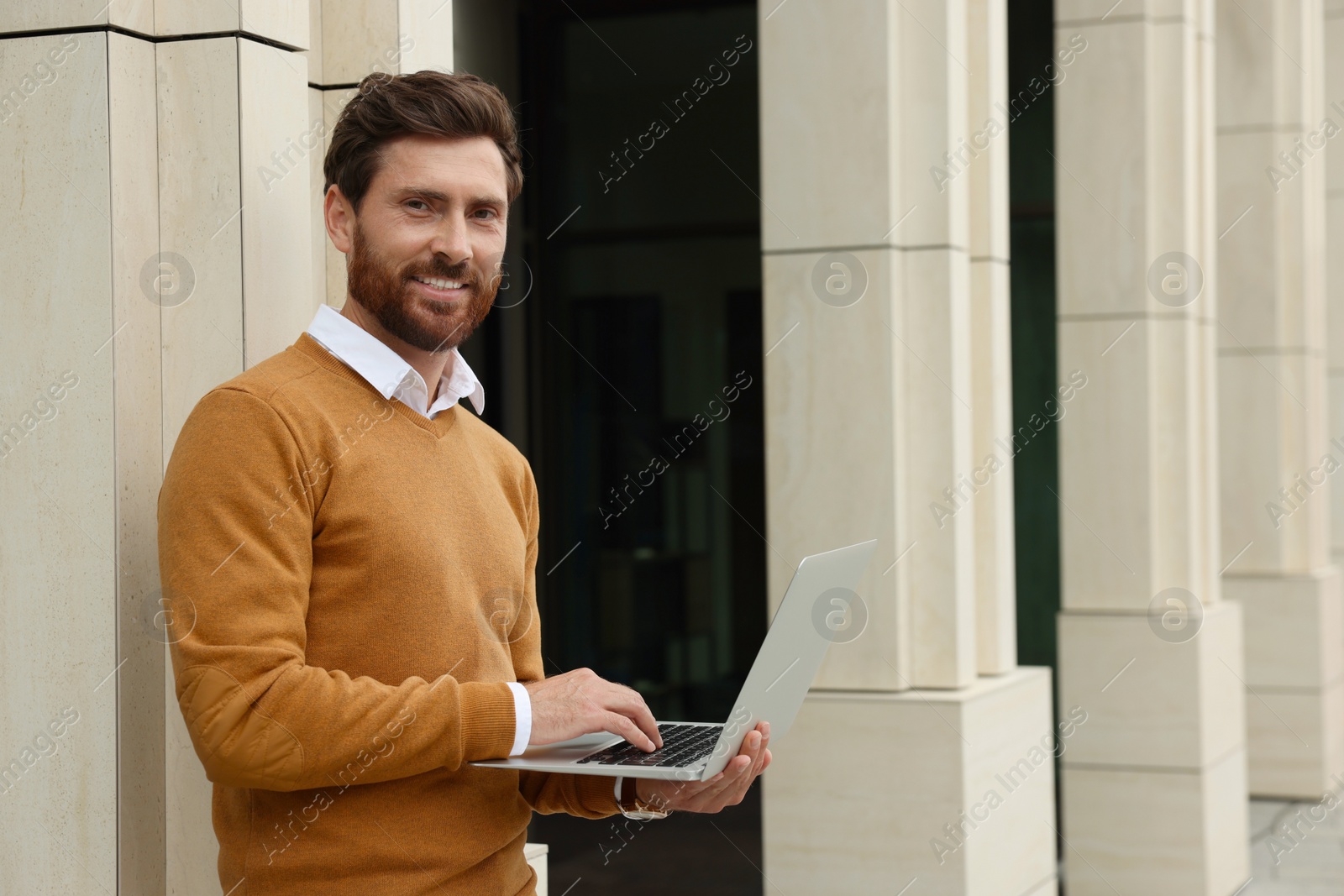 Photo of Handsome man with laptop near building on city street