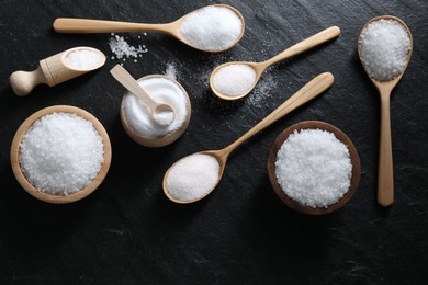 Photo of Organic white salt in bowls and spoons on black table, flat lay