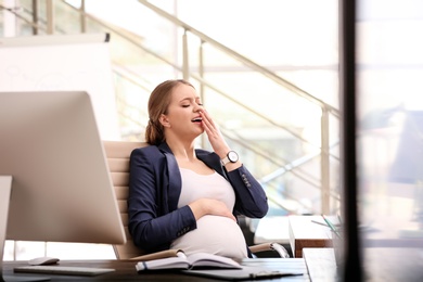 Photo of Young pregnant woman feeling tired while working in office