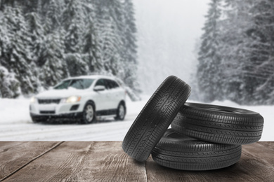 Image of Snow tires on wooden surface and winter landscape with car
