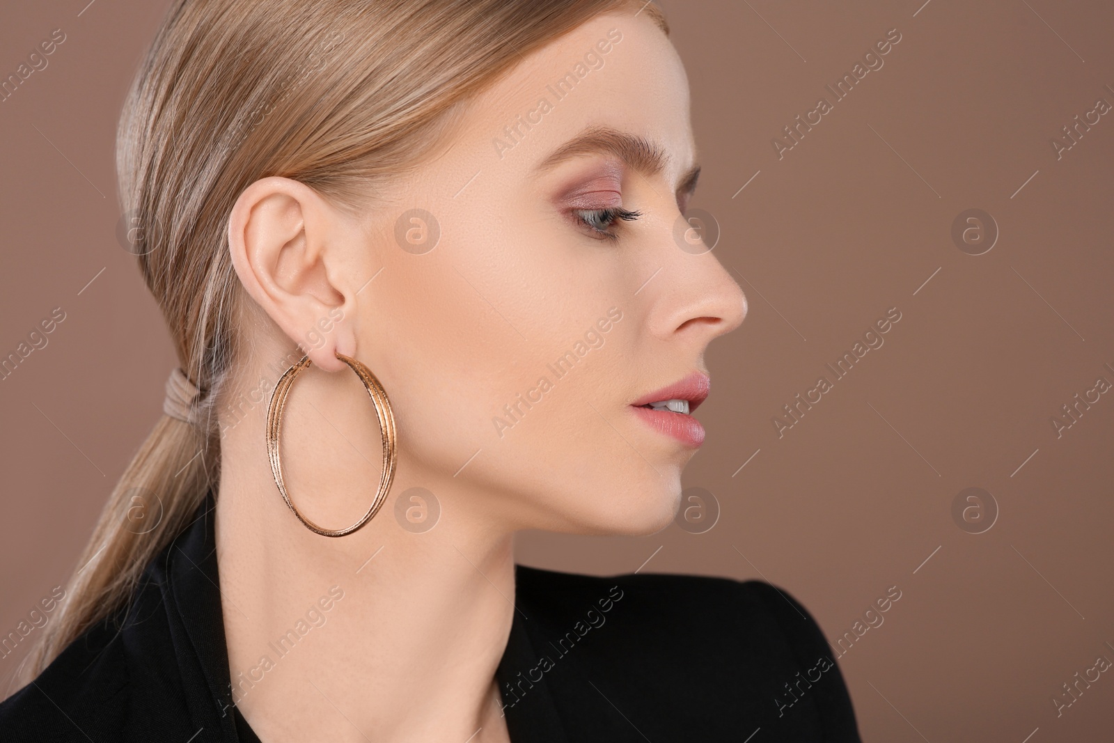 Photo of Beautiful young woman with elegant earrings on light brown background. Space for text