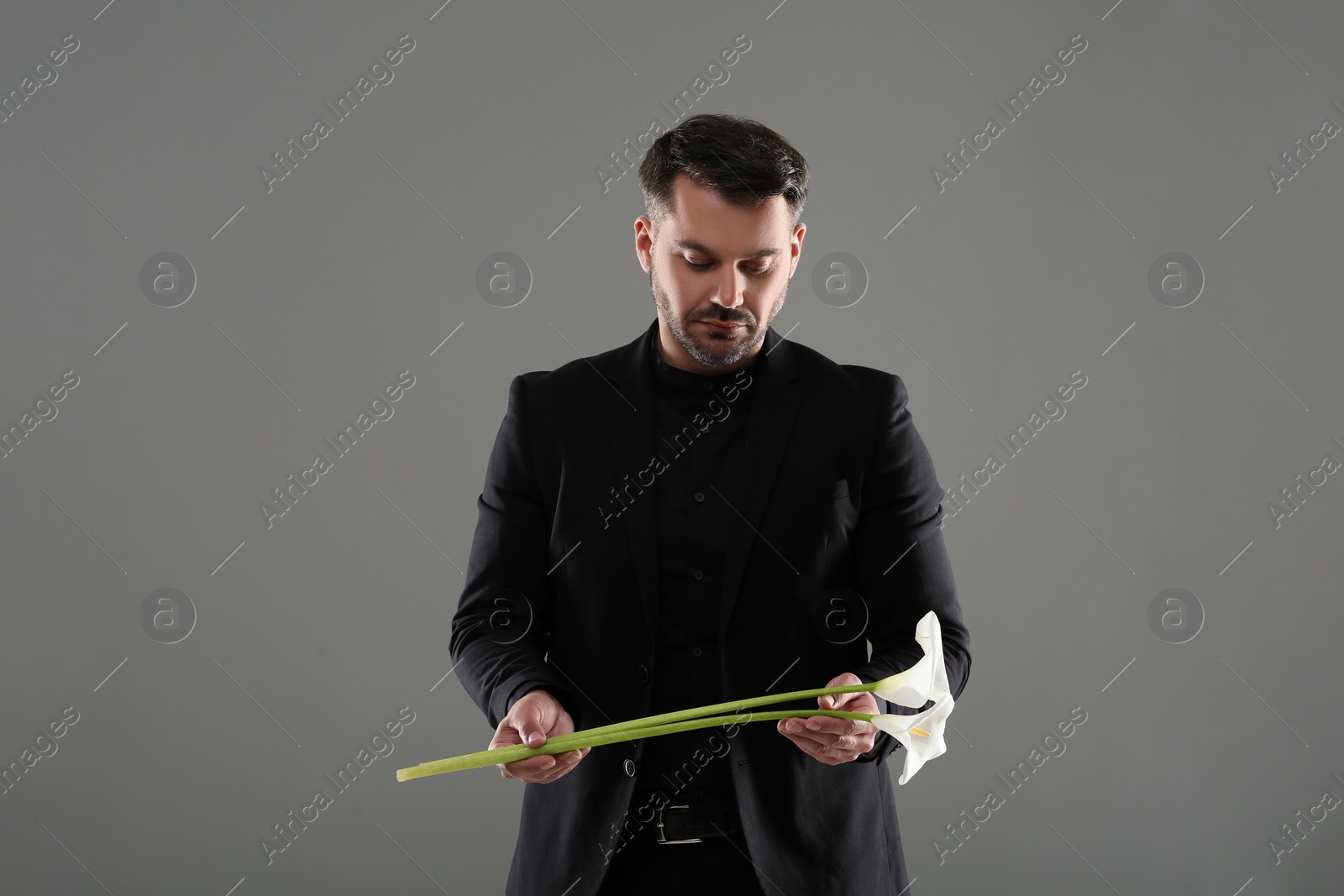 Photo of Sad man with calla lily flower on grey background. Funeral ceremony