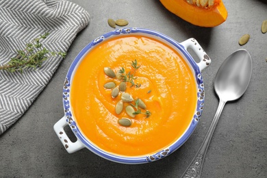 Delicious pumpkin soup in bowl on grey table, flat lay