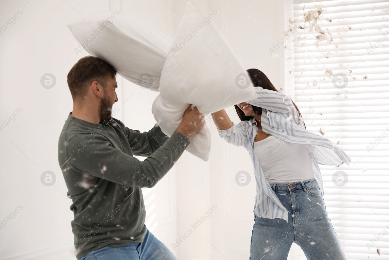 Photo of Happy young couple having fun pillow fight at home