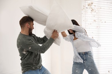 Happy young couple having fun pillow fight at home