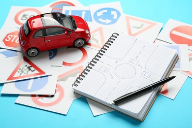 Many different road sign cards, notebook with sketch of roundabout and toy car on light blue background. Driving school