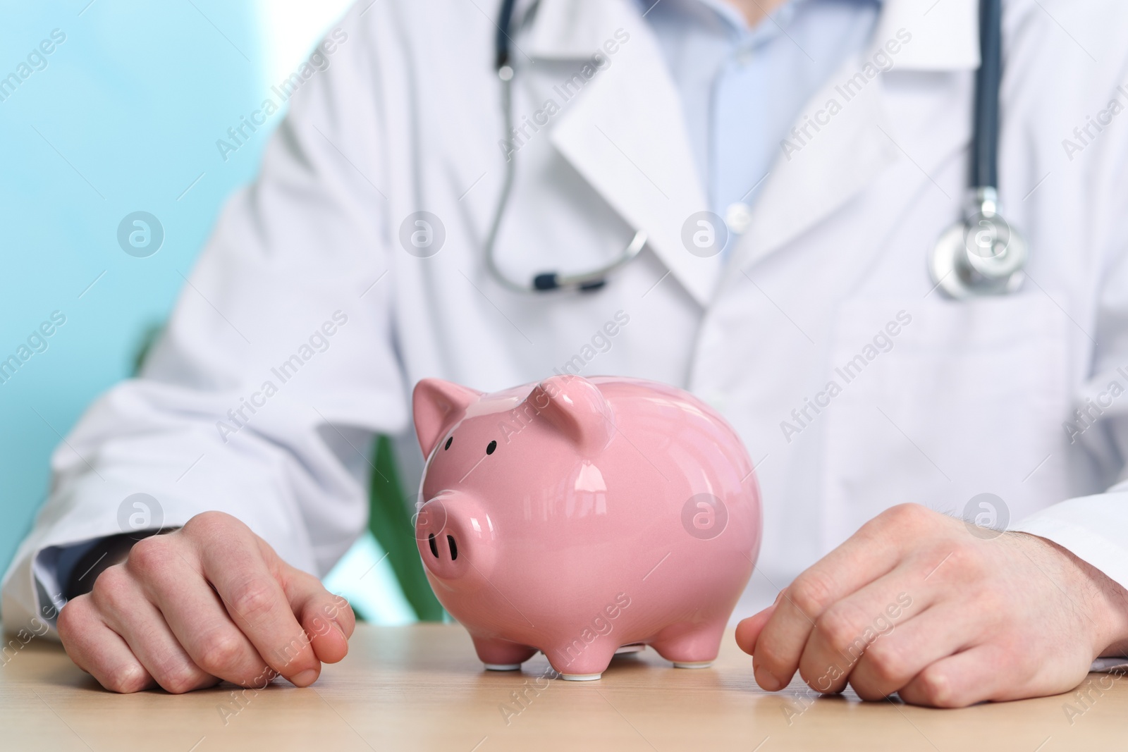 Photo of Doctor with piggy bank at wooden table, closeup