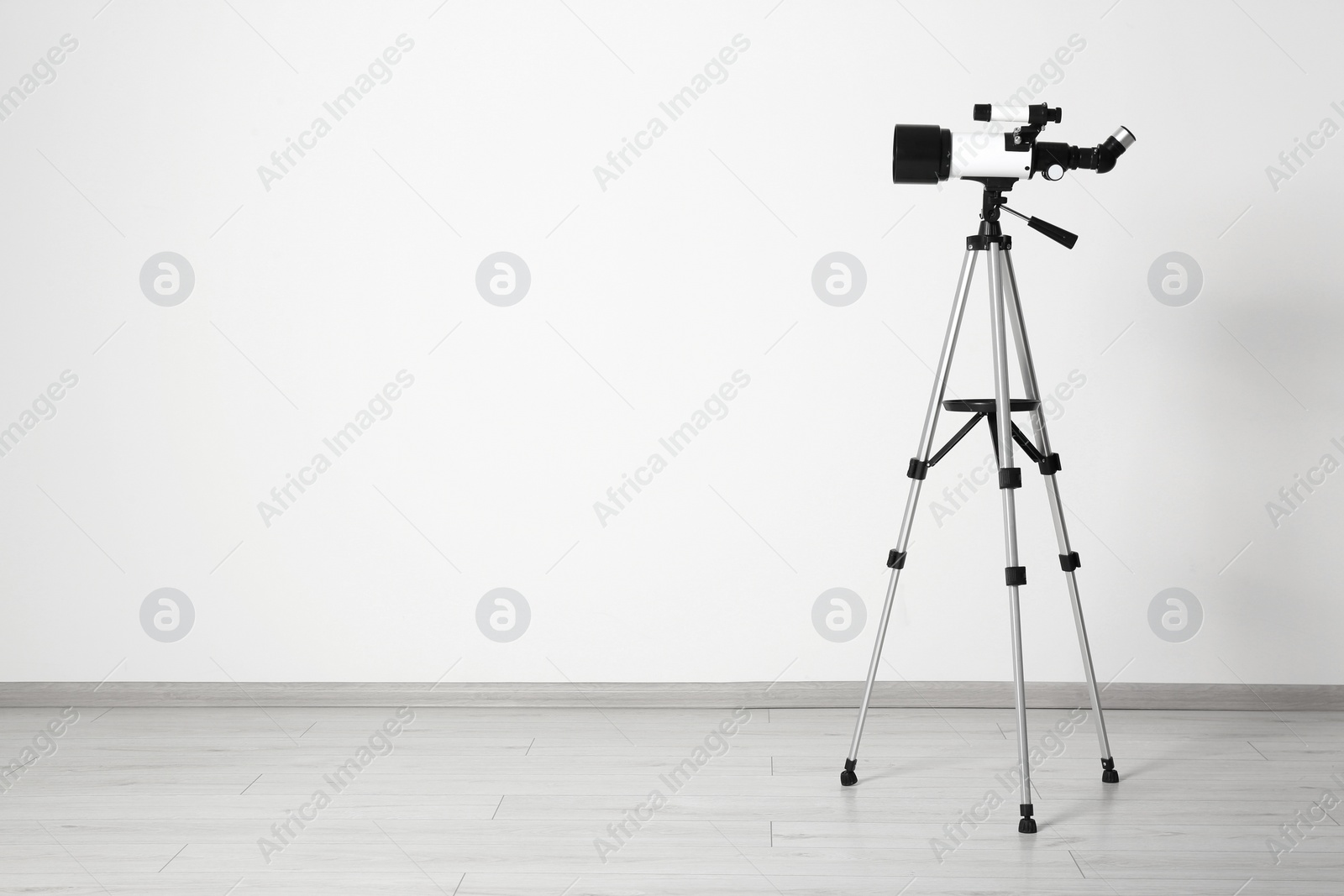 Photo of Tripod with modern telescope near white wall. Space for text