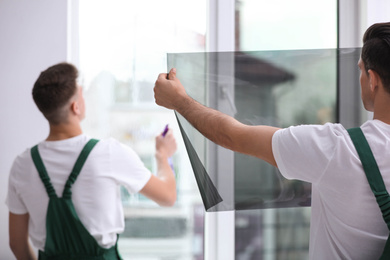 Professional workers tinting window with foil indoors