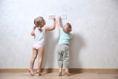 Photo of Little children playing with electrical socket indoors, back view. Dangerous situation