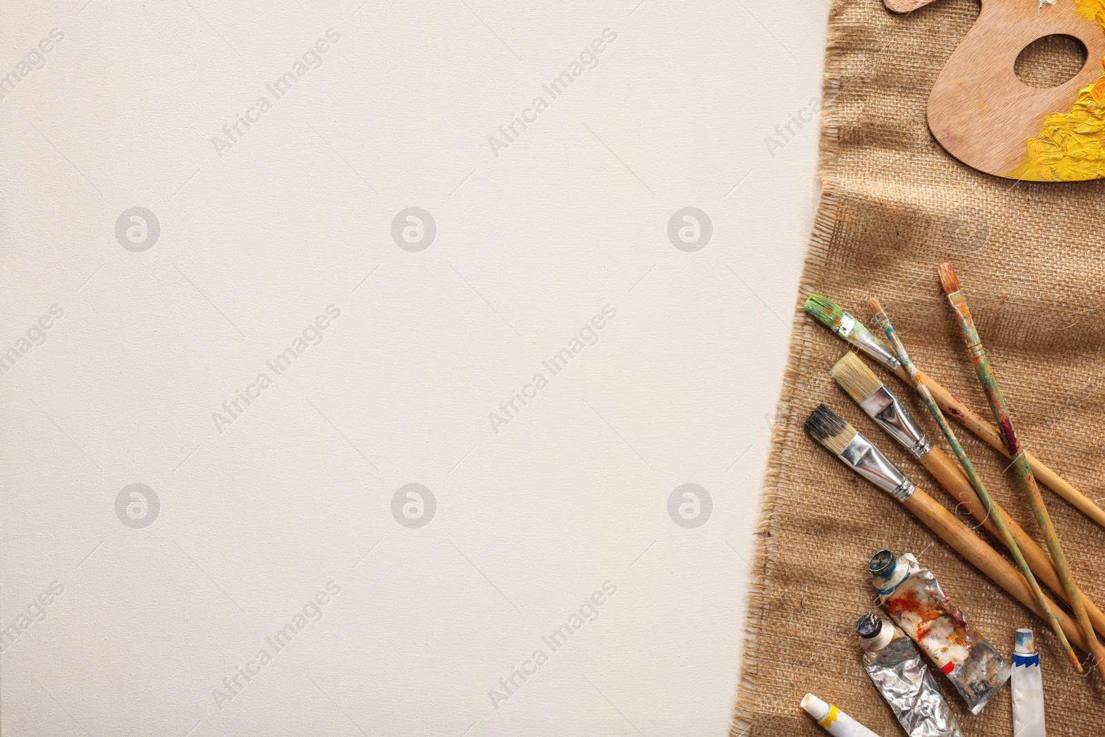 Photo of Natural burlap fabric and different painting supplies on white background, top view. Space for text