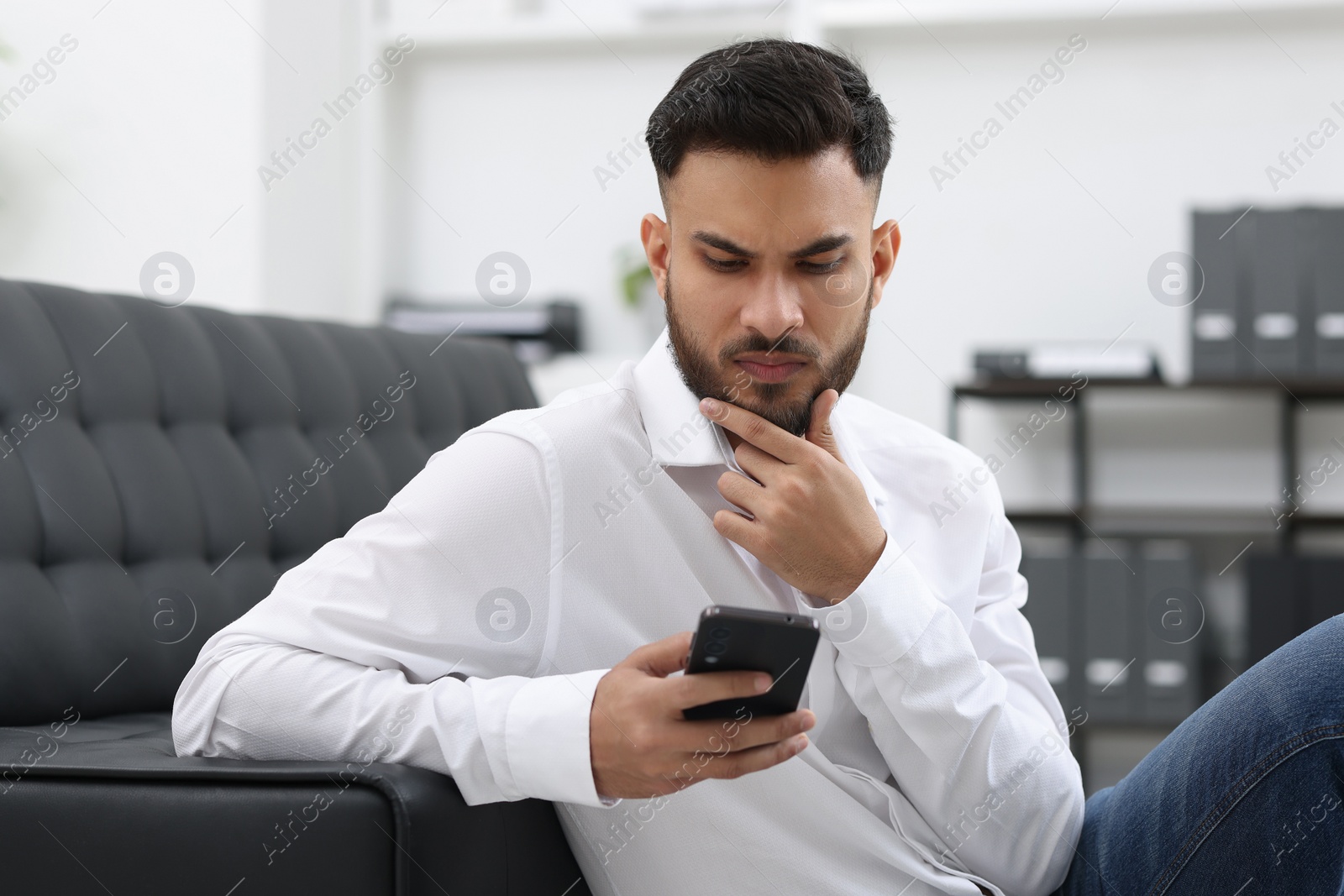 Photo of Handsome young man using smartphone in office