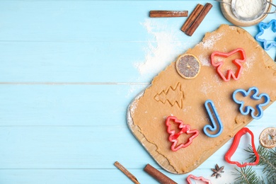 Photo of Raw dough, different cutters and ingredients for Christmas cookies on light blue wooden table, flat lay. Space for text