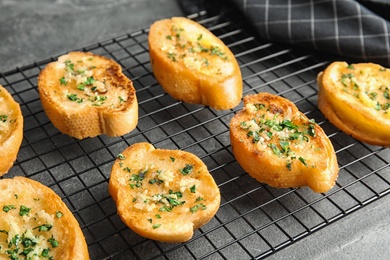 Photo of Baking rack with tasty homemade garlic bread on table, closeup