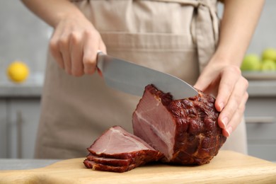 Photo of Woman cutting ham on wooden board at table indoors, closeup