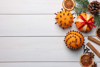 Pomander balls made of tangerines with cloves, spices and fir branches on white wooden table, flat lay. Space for text