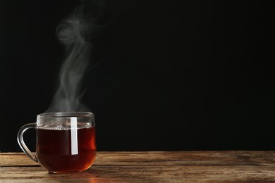 Photo of Cup with steam on wooden table against black background. Space for text