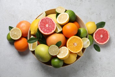 Different fresh citrus fruits and leaves in bowl on light textured table, flat lay