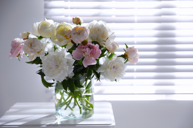 Beautiful peonies in vase on table near window indoors