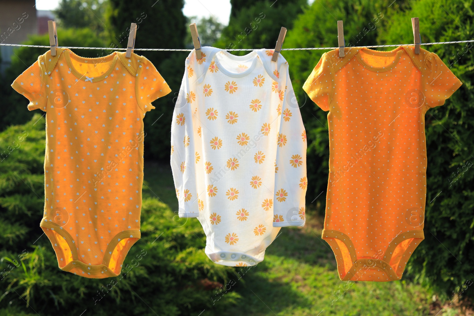 Photo of Clean baby onesies hanging on washing line in garden. Drying clothes