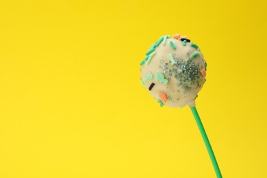 Photo of Delicious confectionery. Sweet cake pop decorated with sprinkles on yellow background, closeup. Space for text