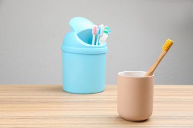 Natural bamboo toothbrush and plastic ones in toy trash can on wooden table