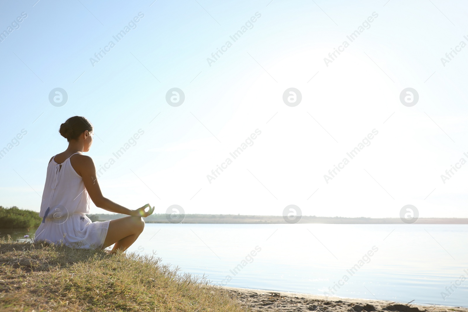 Photo of Young woman meditating near river at sunset, space for text. Nature healing power