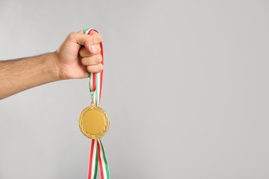 Photo of Man holding golden medal on grey background, closeup. Space for design