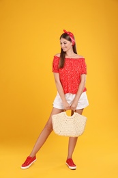 Photo of Beautiful young woman with stylish straw bag on yellow background