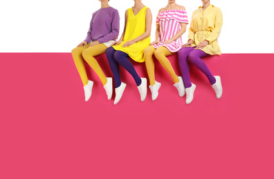 Group of women wearing bright tights and stylish shoes sitting on color background, closeup