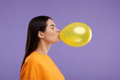 Photo of Woman inflating yellow balloon on purple background