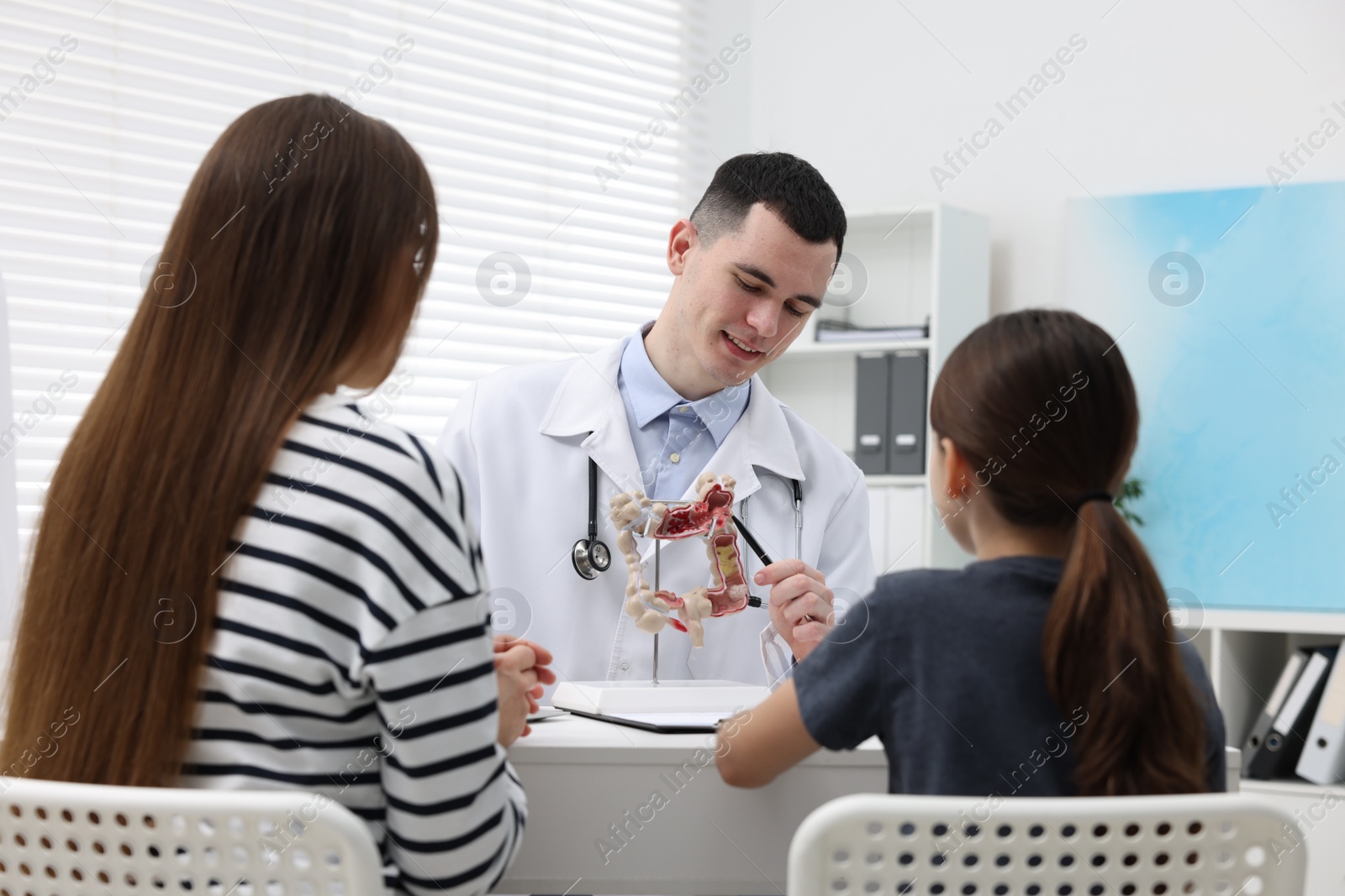 Photo of Gastroenterologist with model of intestine consulting woman and her daughter in clinic