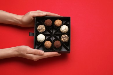 Photo of Woman with box of delicious chocolate candies on red background, top view