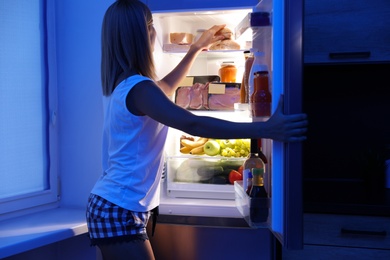 Woman taking products out of refrigerator in kitchen at night