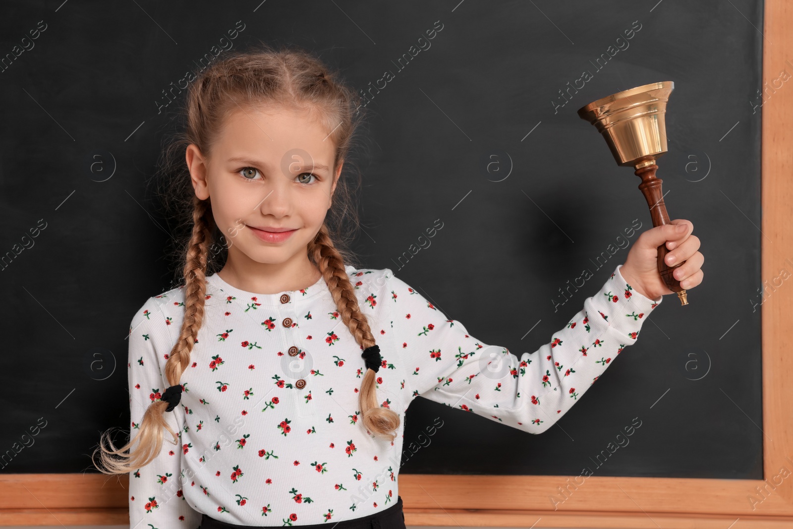 Photo of Pupil with school bell near black chalkboard in classroom